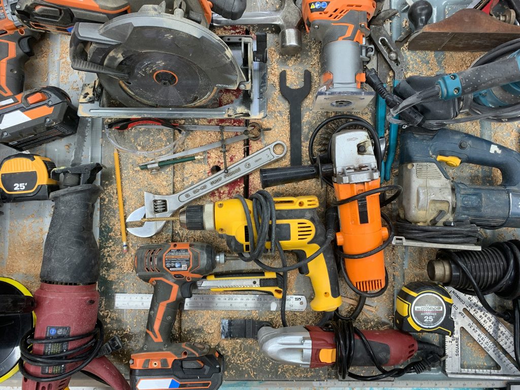 A top-down view of various power tools and hand tools scattered on a dusty workbench.