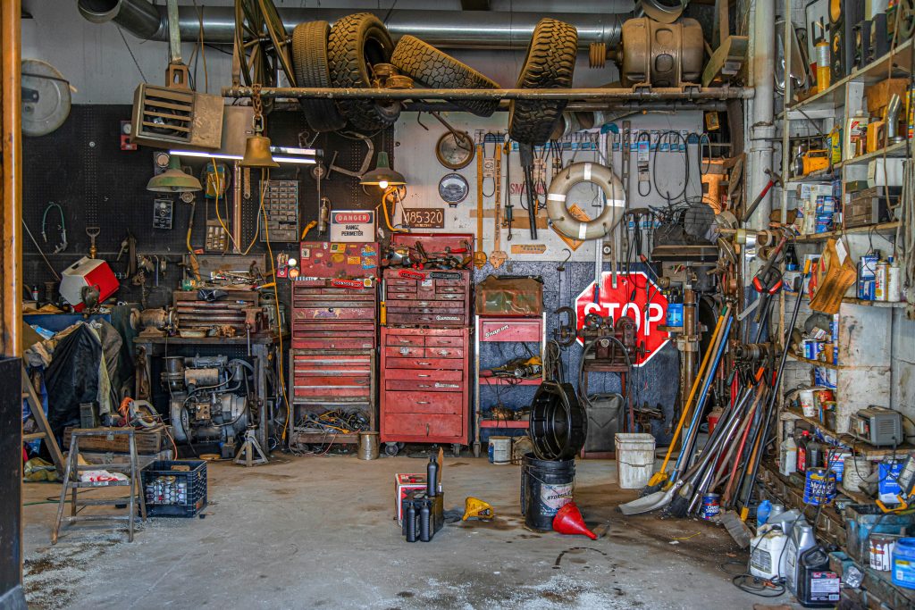 A cluttered and colorful mechanic’s garage with tools, tires, and toolboxes.