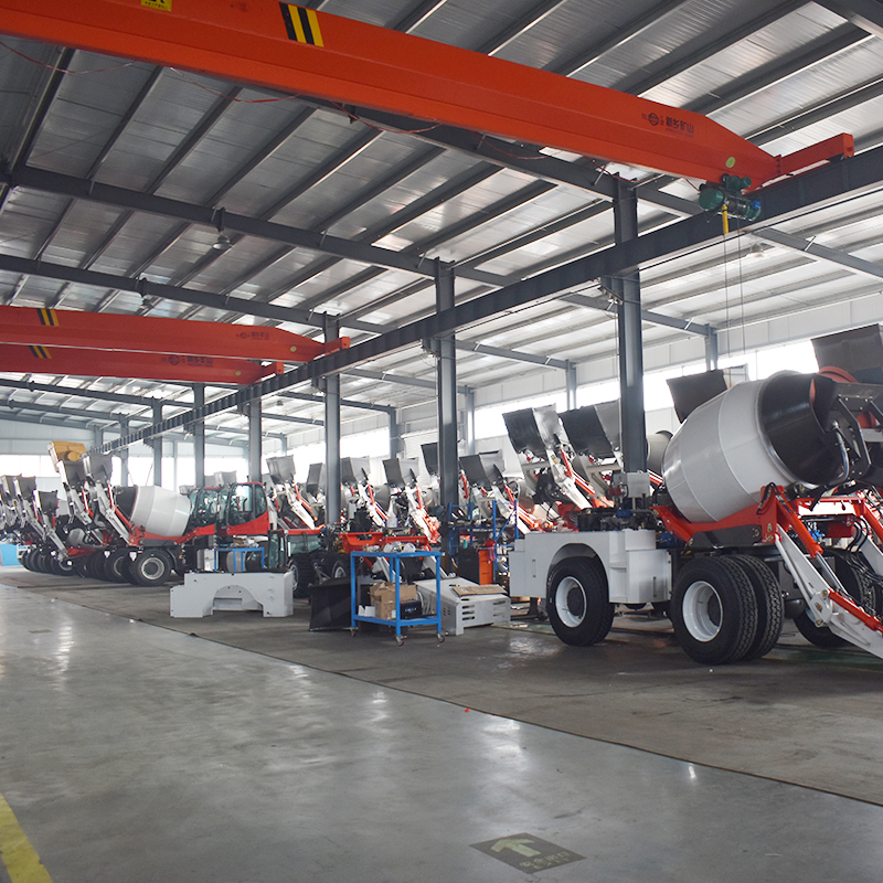 Deretan truk mixer beton self-loading di dalam pabrik manufaktur berat dengan crane gantung.